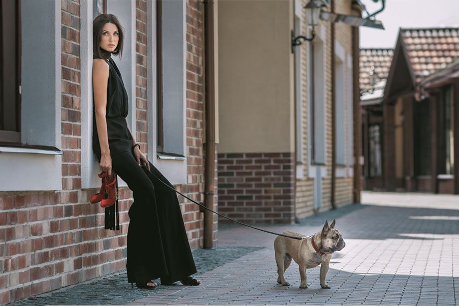 Žena u elegantnom crnom kombinezonu sa crvenim cipelama i psom.